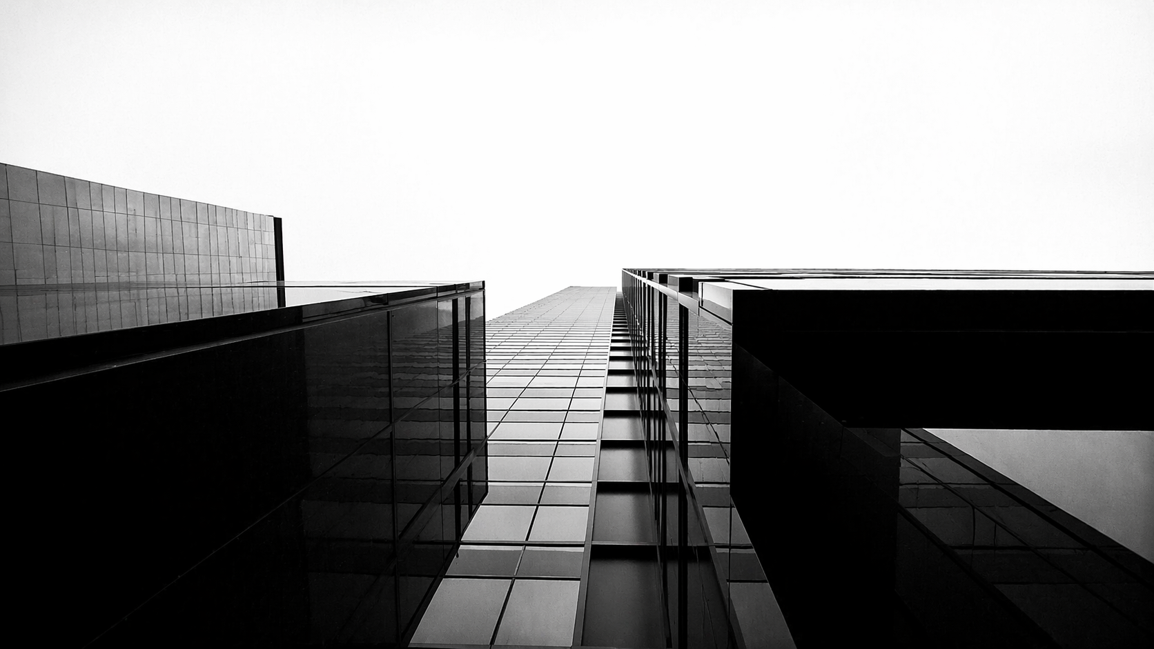 Low-angle black and white photograph of modern glass skyscrapers from below, bright sky at center. Home hero background.