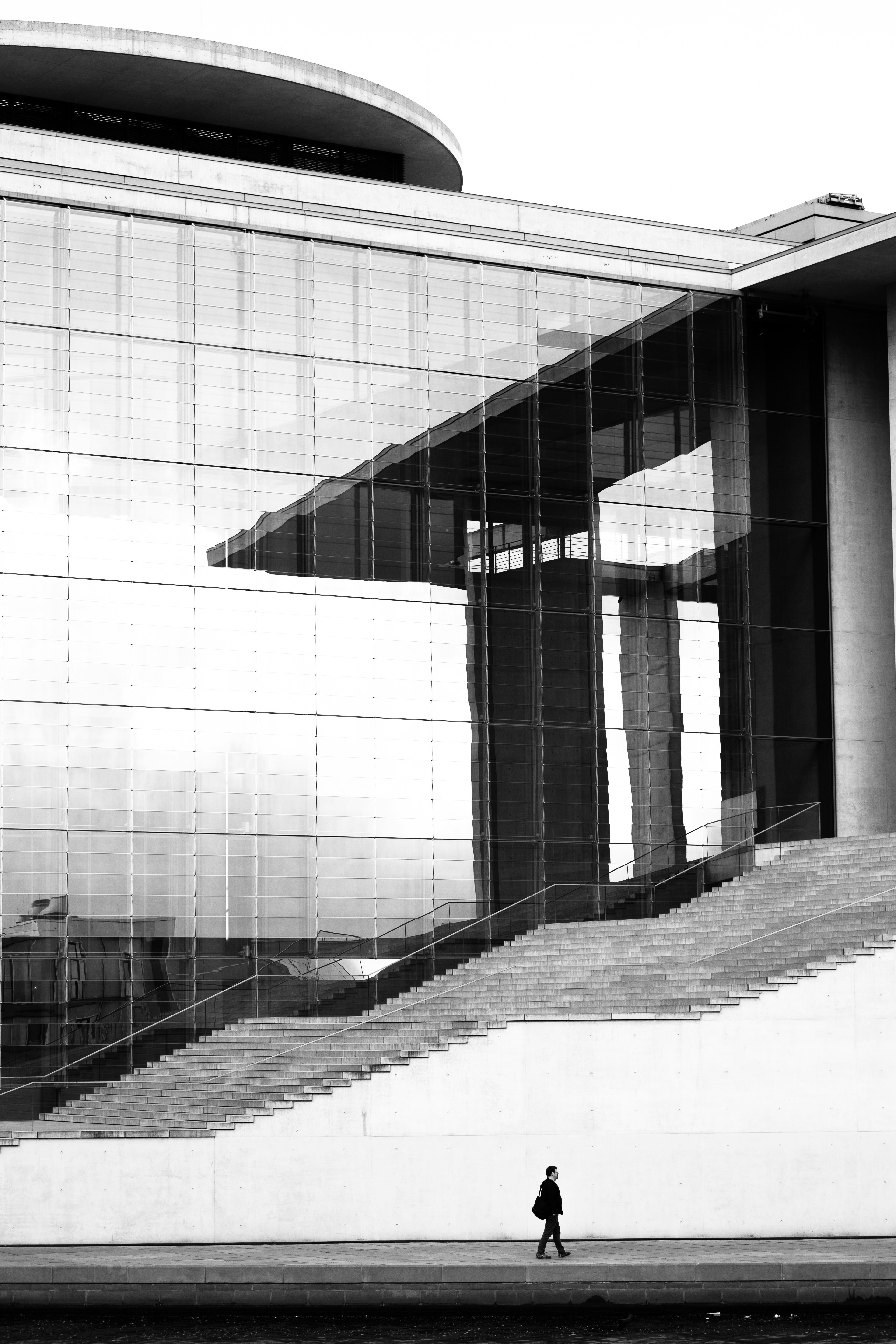 Black and white exterior of a modern building with glass curtain wall, wide stone stairs, and strong vertical lines.